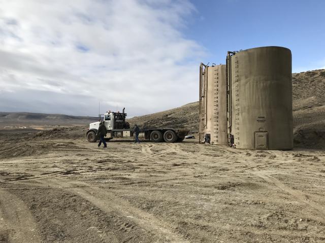 a pair of men, a flatbed truck, and two large storage tanks