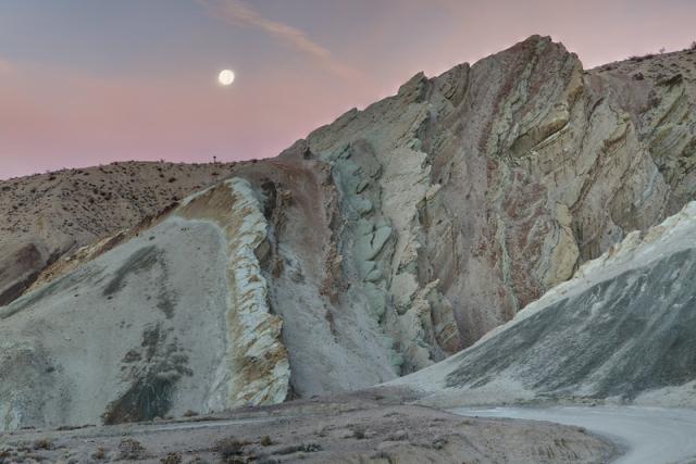 the moon rises over a multicolored rock face.