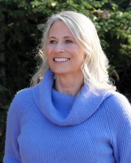 A professional headshot of a woman with blond hair wearing a blue sweater.