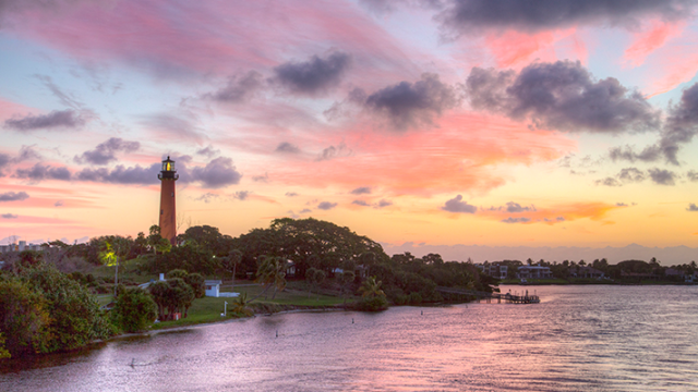 A red lighthouse stands next to a body of water at sunset.