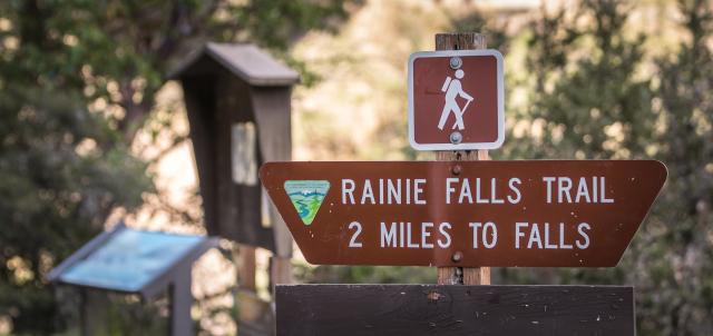 A brown and white trail marker that reads Rainie Falls Trail 2 Miles to Falls.