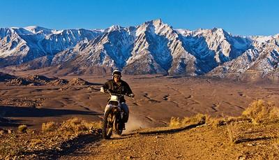 A dirtbike on a trail with tall snowy mountains in the background