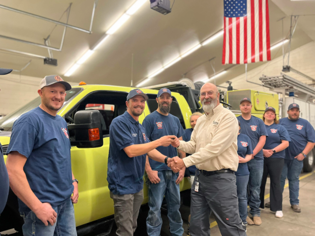 A group of Caucasian men and women smile in front of a large yellow truck