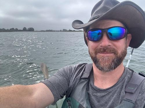 A man in glasses and a hat takes a selfie on a kayak