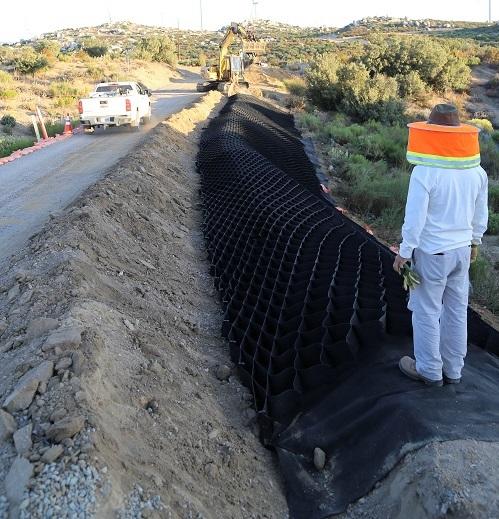 A man in safety gear stands over black netting lining a trench