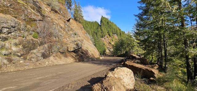 Road showing cleaned up rockslide area with barriers at the base of the previously disturbed slope