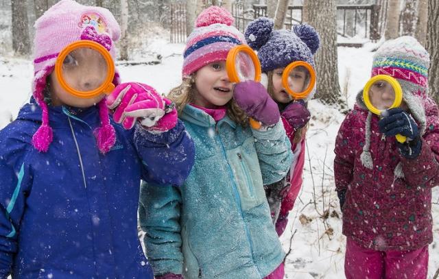 Kids in a snowy forest look through magnifying glasses