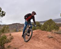 A biker riding on a red dirt trail with trees and rough terrain surrounding them. 