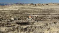 rolling Wyoming sagebrush landscape in shades of tan with a oil pump jack and tanks painted to blend.