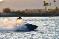 a person wearing a helmet on a jetski in Lake Havasu. a large wave of water is visible to the side of and behind the rider