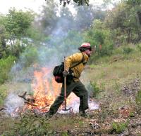 Man in hard hat and yellow uniform holding a tool maintains a burn. 