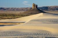 A tall rock column rises above white sand dunes.