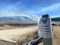 A sign on a fencepost reads prescribed burn area with smoke in background. 