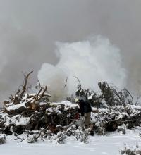 A firefighter ignites a slash pile surround by snow. 