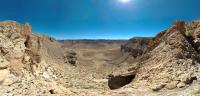 A birds eye view of a remote, tranquil desert with towering canyon walls and a dry streambed meandering through the valley below.