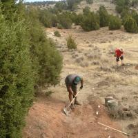 Two people are using tools to improve a dirt trail.