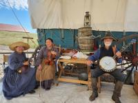 Pioneer re-enactors with musical instruments sit next to a wagon. 