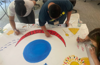 Three students paint a small mural.