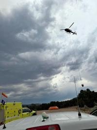 A helicopter flies above green wildland fire trucks preparing to drop a bucket of water on a wildland fire.