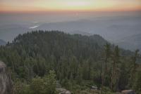 A sunsets over a valley with tall sequoia trees in the foreground.