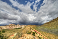 Red rock and sagebrush landscape under a blue sky with white clouds.