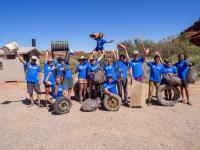 a group of people in blue t-shirts stand with trash collected off public lands.