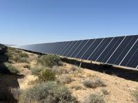 A solar array on flat land with scattered vegetation.