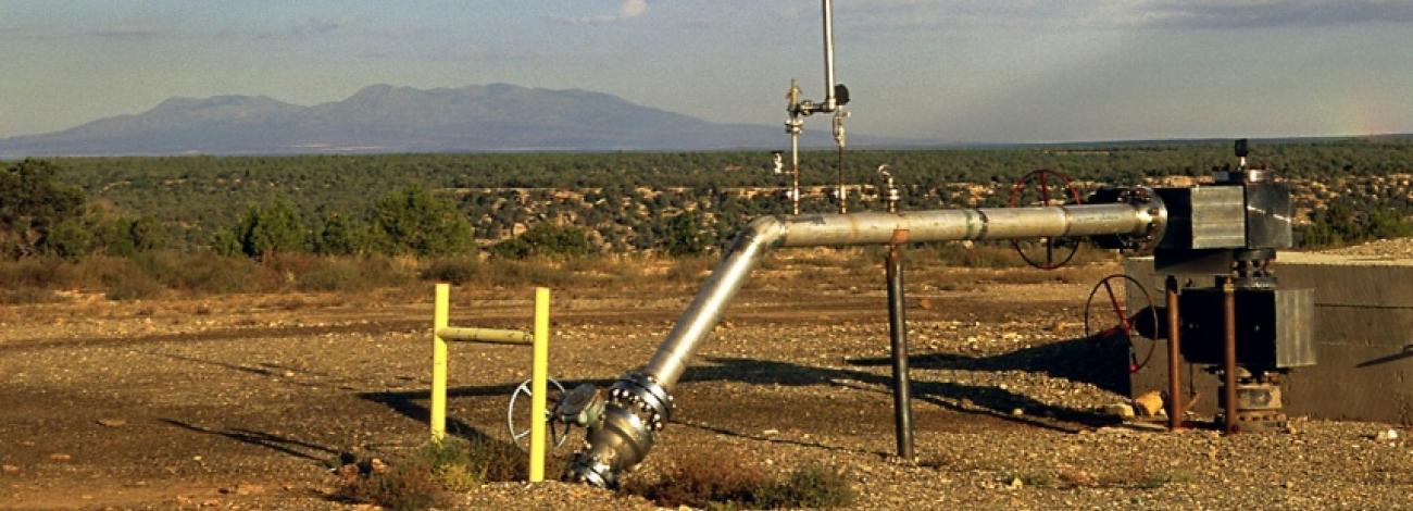 Oil well in Colorado with rainbow appearing over head with partly cloudy skies.