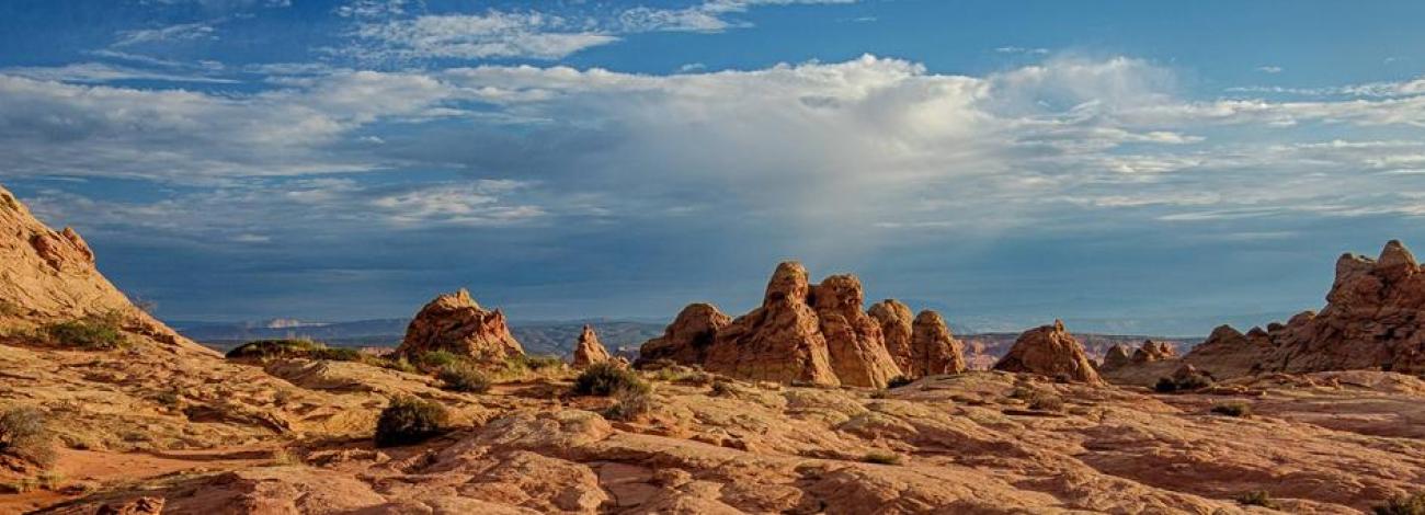 Coyote Buttes North sandstone features. Vast landscape of sandstone with sandstone teepees in the distance and a beautiful blue sky with a touch of clouds.