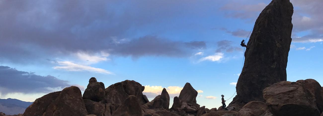 Pair of Climbers repelling down rock face while one partner belays 