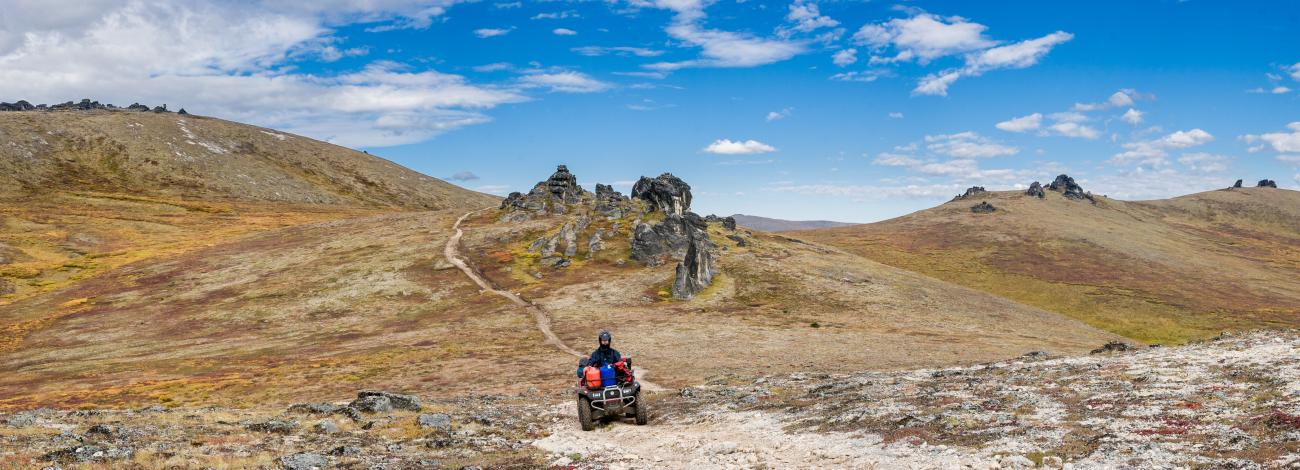 A rider on an ATV navigates a rocky trail through a treeless mountain valley.