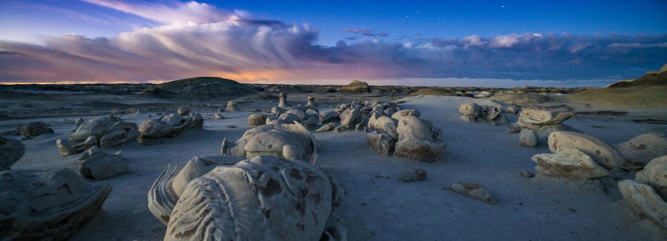 A photo taken during early morning light, of large rocks that look like eggs, with sandy ground and blue skies and clouds in the background.