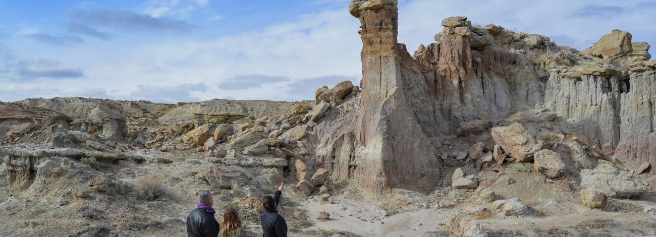 Three people stand on a trail looking at an interesting geological formation called a hoodoo.