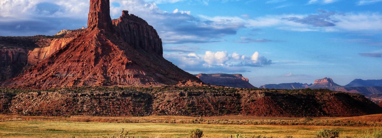 A spire of sandstone and adjoining cliffs stand tall above yellow grasses.