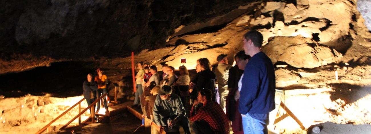 A group of people view the depth of a cave from behind a safety rail. BLM photo.