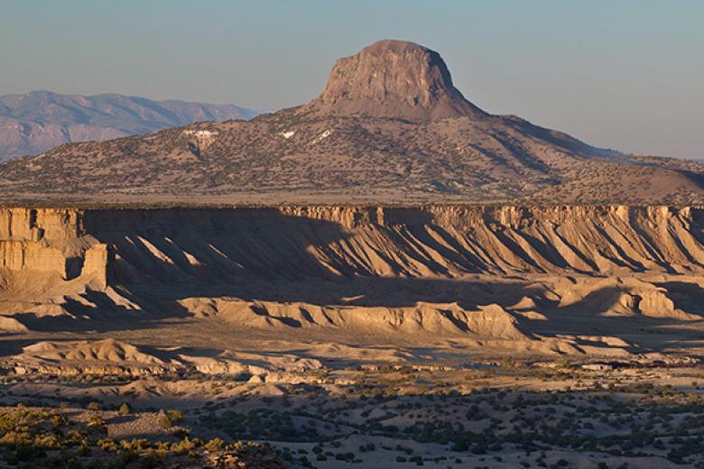 The volcanic plug of Cabezon Peak with long shadows on the cliffs in the foreground.