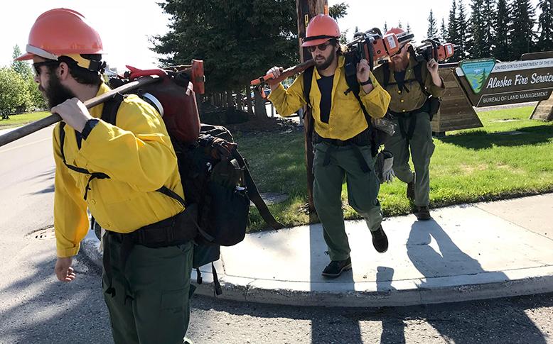 Men walking with chainsaws and other tools over shoulder.