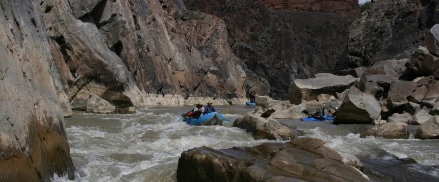 Recreators rafting and kayaking down a semi choppy rapid near the bottom of a cliff