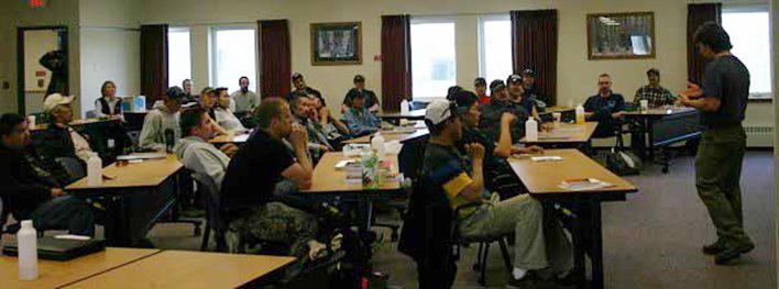 Trainer in front of large conference room with fire personnel sitting listening.