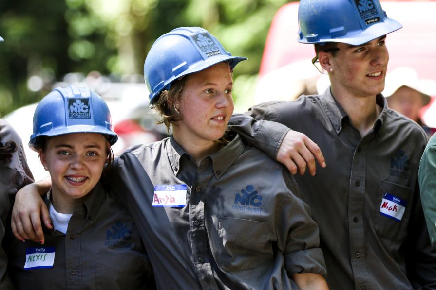 Three youths wearing coveralls and blue hard hats standing shoulder to shoulder posing for a photograph