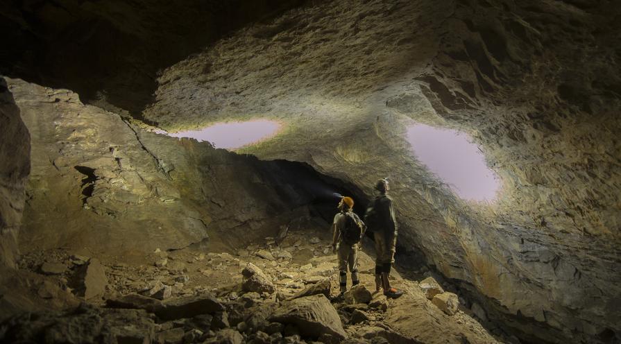 Two men shine their headlamps up at the ceiling of Bloomington Cave.