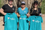 Three volunteers stand together displaying their t-shirts for cleanup efforts.