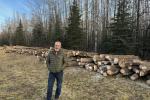 Caucasian man smiles in front of cut stacked logs 