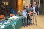 Two men and three boys in baseball caps pose in front of a table holding a model T. rex skull. 