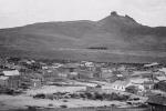 An Old West mining town with wooden building in the foreground and a hill in the distance.