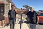 Two men stand near a campground host sign