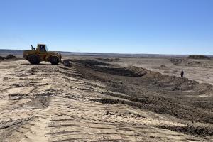 A bulldozer moves dirt. A large area in the foreground is already scraped away.