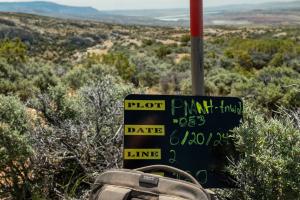 photo: small blackboard with writing propped on a backpack leaning on a shovel overlooking shrub-covered hills